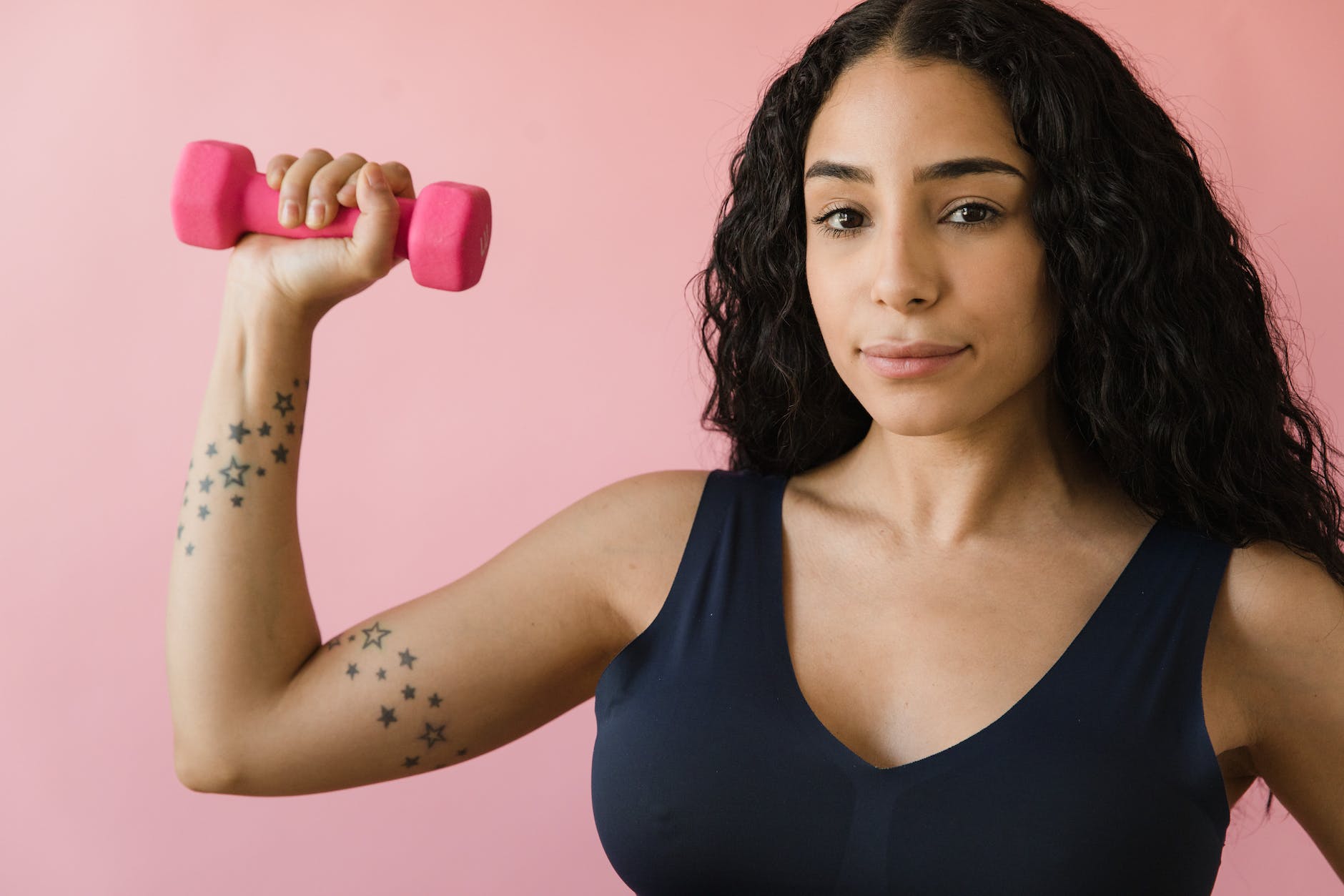 woman in blue tank top holding a pink dumbbell